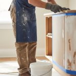 Artisan préparant une surface pour peinture avec des outils dans un intérieur lumineux.